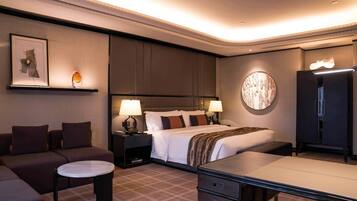 Quarto de hotel moderno com uma cama grande, duas mesas de cabeceira com luminárias, um sofá, uma mesinha redonda e um armário.