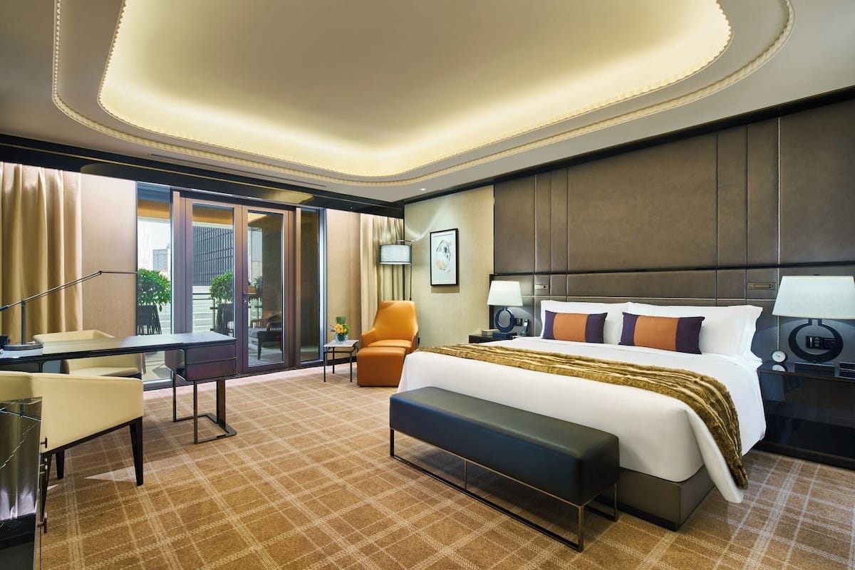 A hotel room with a large bed, a desk, a chair, and a view of the outdoors.