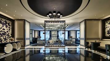 Un elegante vestíbulo de hotel con piso reflectante, una imponente lámpara de cristal y una zona de estar con sofás y bar.