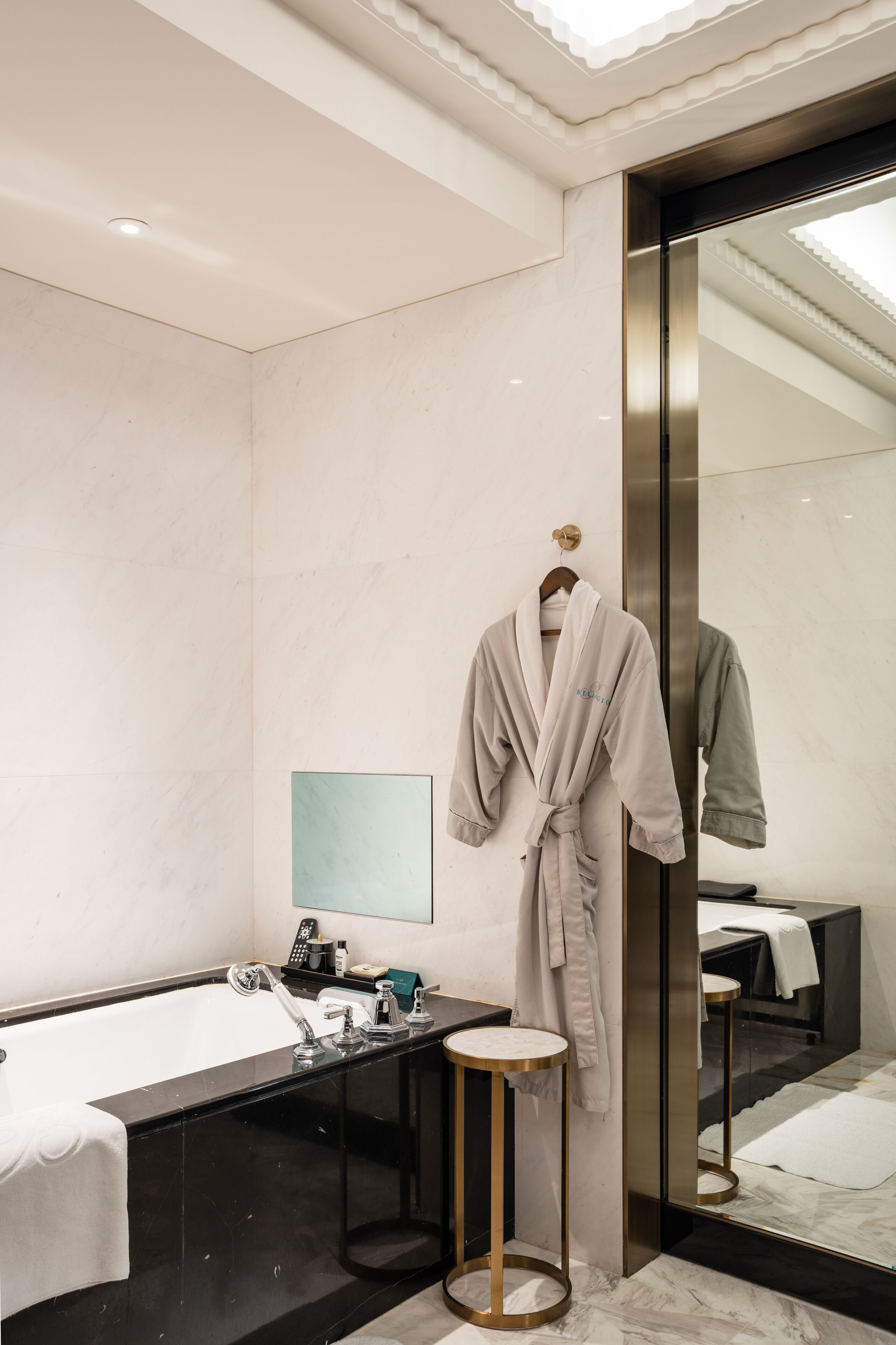 Un baño moderno con un espejo grande, una bañera, un lavamanos y una bata colgada en un perchero.