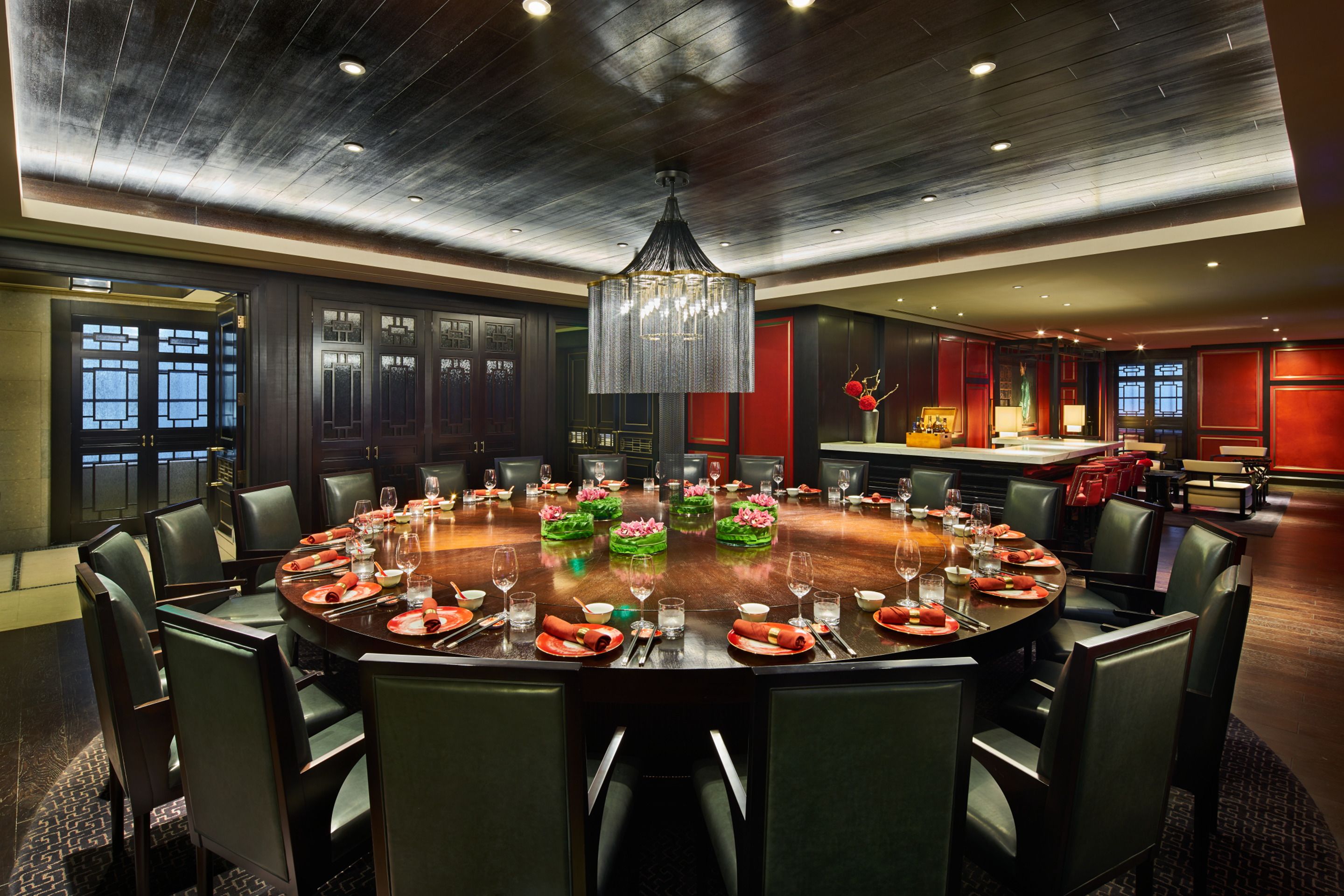 A large round table set for a meal with chairs around it, in a room with dark wood paneling and a chandelier.