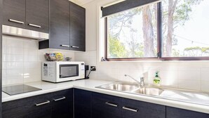 A modern kitchen with dark cabinets, a white countertop, a stainless steel sink, and a window with a view of trees. - Kookaburra Retreat (Berowra Heights)
