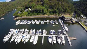 An aerial view of a marina with numerous boats docked, surrounded by lush green hills. - Kookaburra Retreat (Berowra Heights)