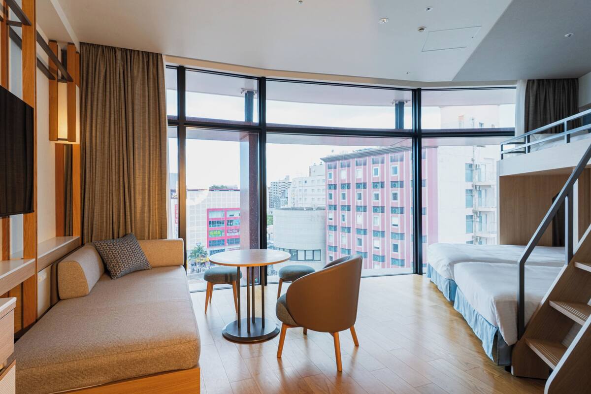 Una habitación de hotel moderna con un ventanal grande, un sofá, una mesita y una cama.