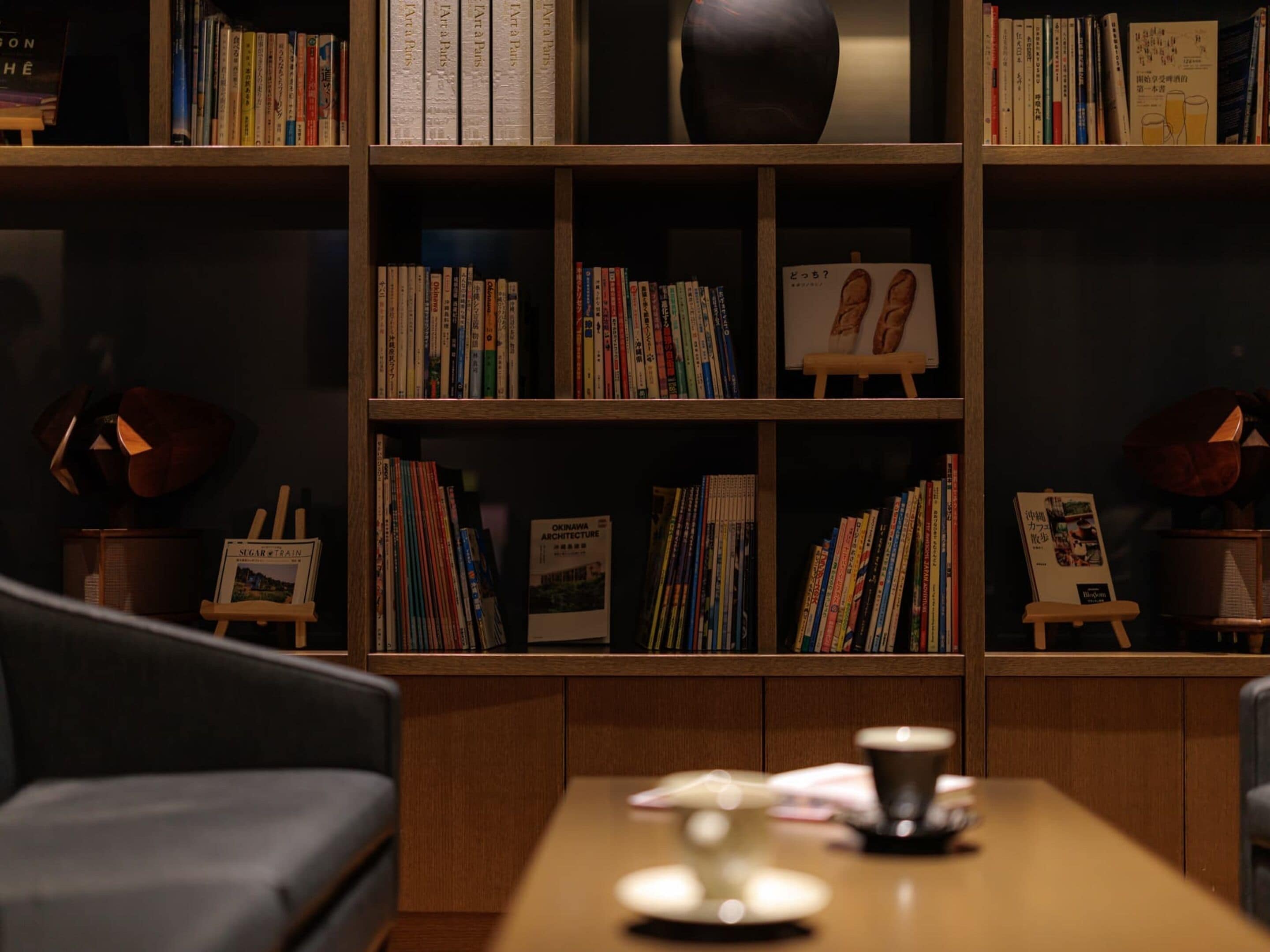 A cozy reading nook with a wooden bookshelf filled with books, a small easel with a painting, and a coffee table with a cup.