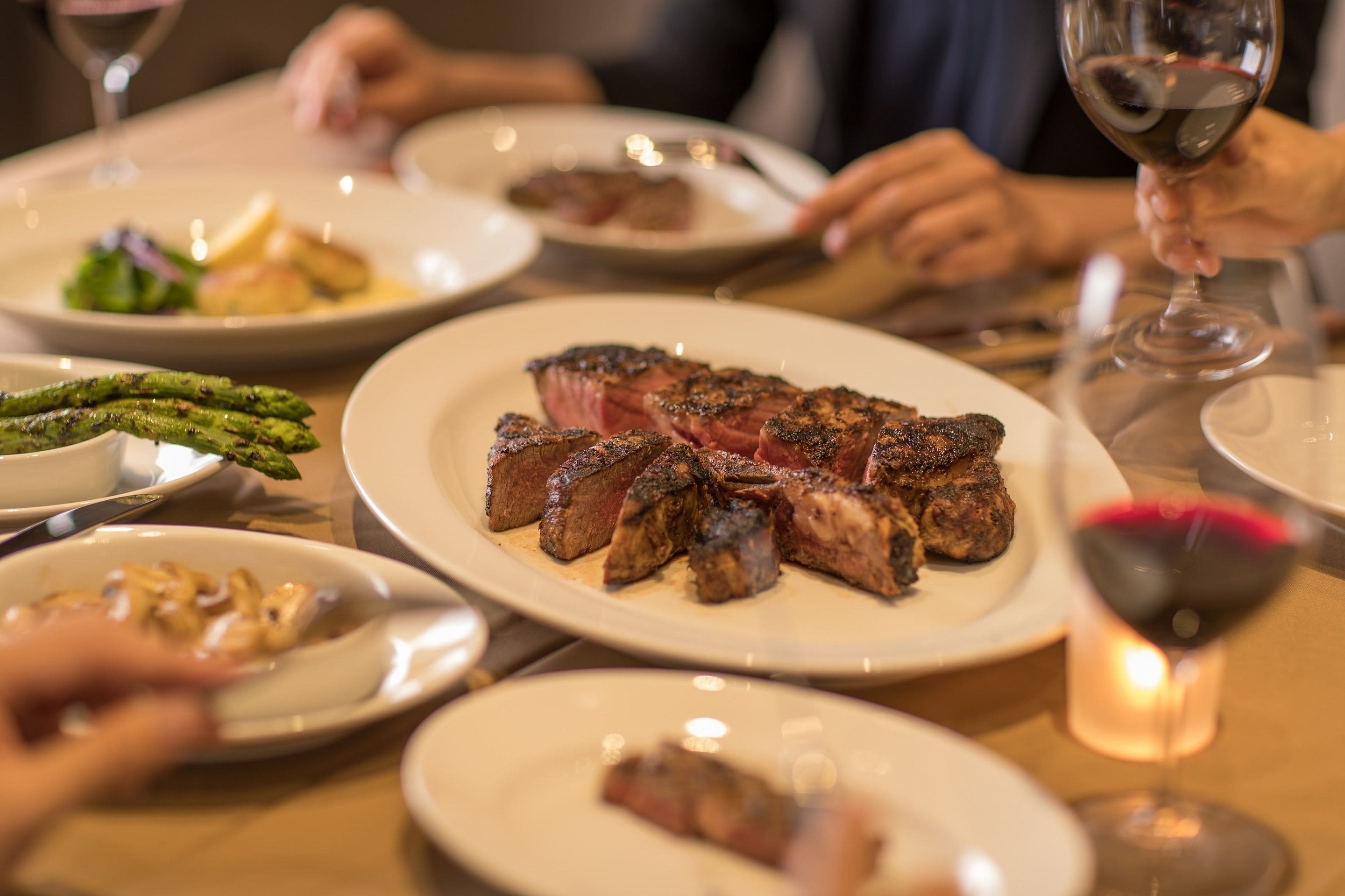Une table à manger avec des assiettes remplies de nourriture, notamment des steaks et des asperges.