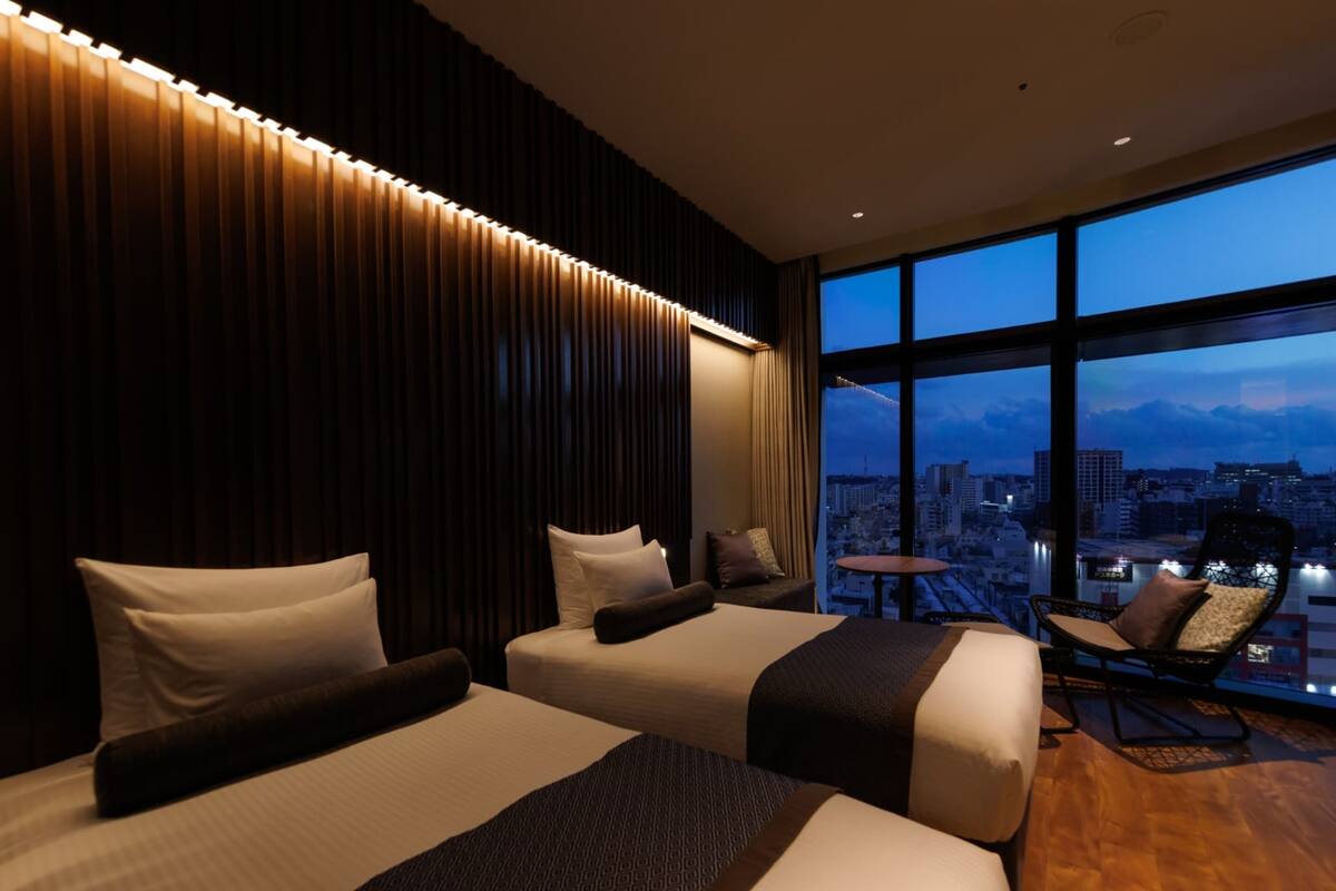 Habitación de hotel con dos camas, vistas a la ciudad y un balcón con una silla.