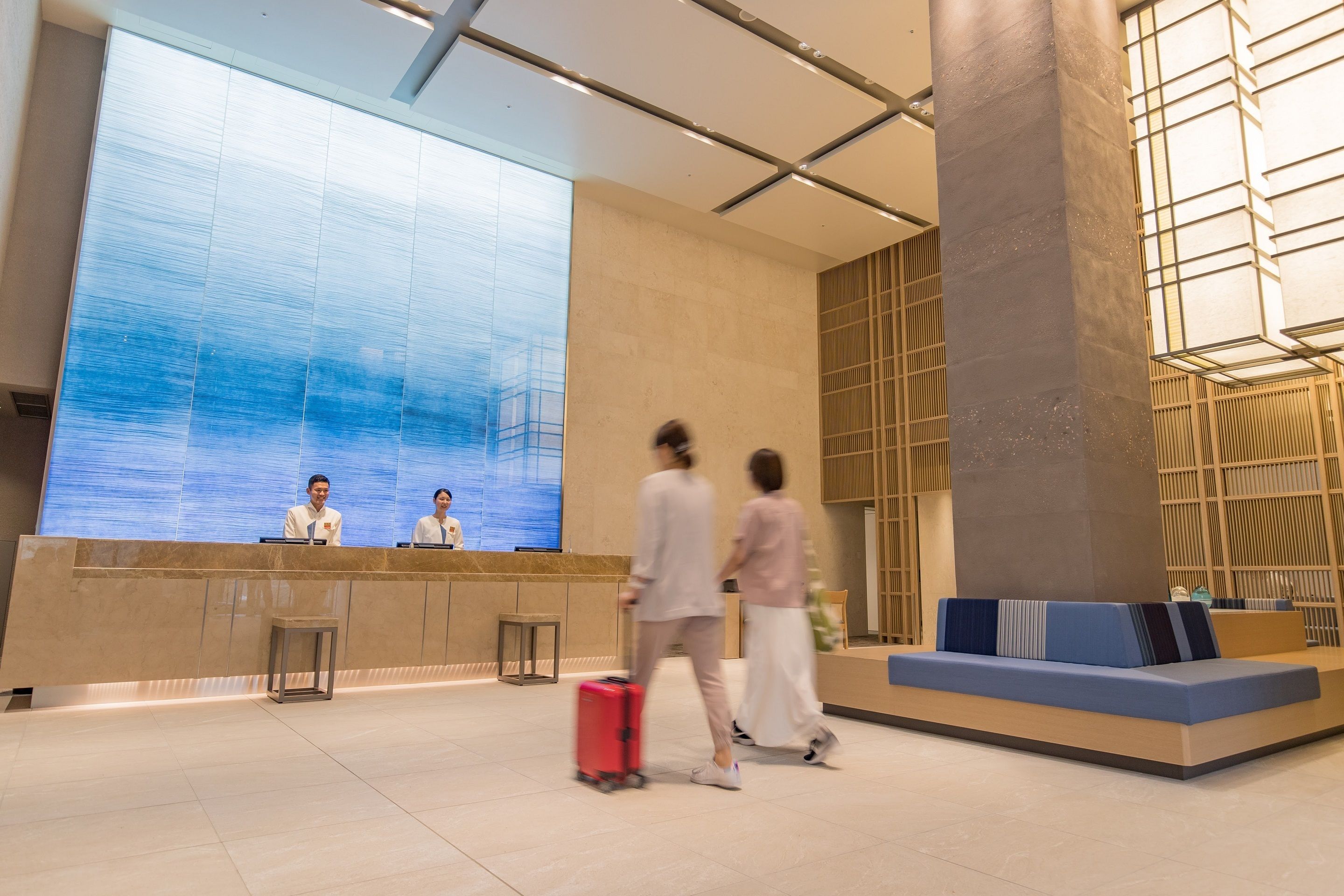 Un área de recepción de hotel moderna con una gran pantalla digital, un mostrador de recepción y un área de descanso.