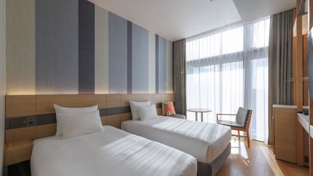 Ein Hotelzimmer mit zwei Betten, einem kleinen Tisch, einem Stuhl und einem Fernseher.