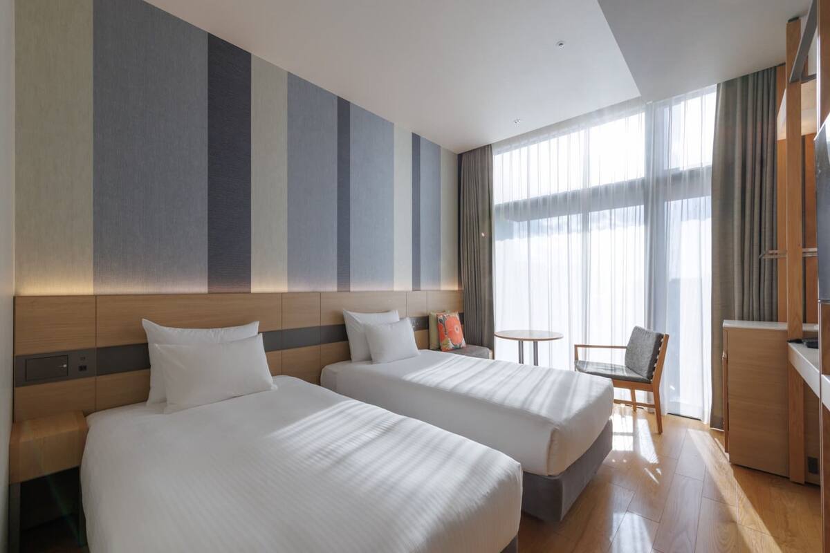 Una habitación de hotel con dos camas, una mesita, una silla y un televisor.
