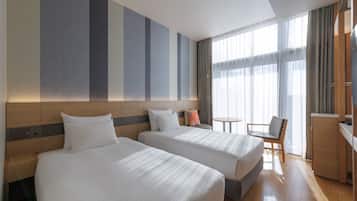 A hotel room with two beds, a small table, a chair, and a TV.
