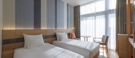 A hotel room with two beds, a small table, a chair, and a TV.