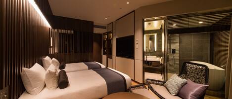 A modern hotel room with two beds, a sitting area, and a bathroom with a bathtub.