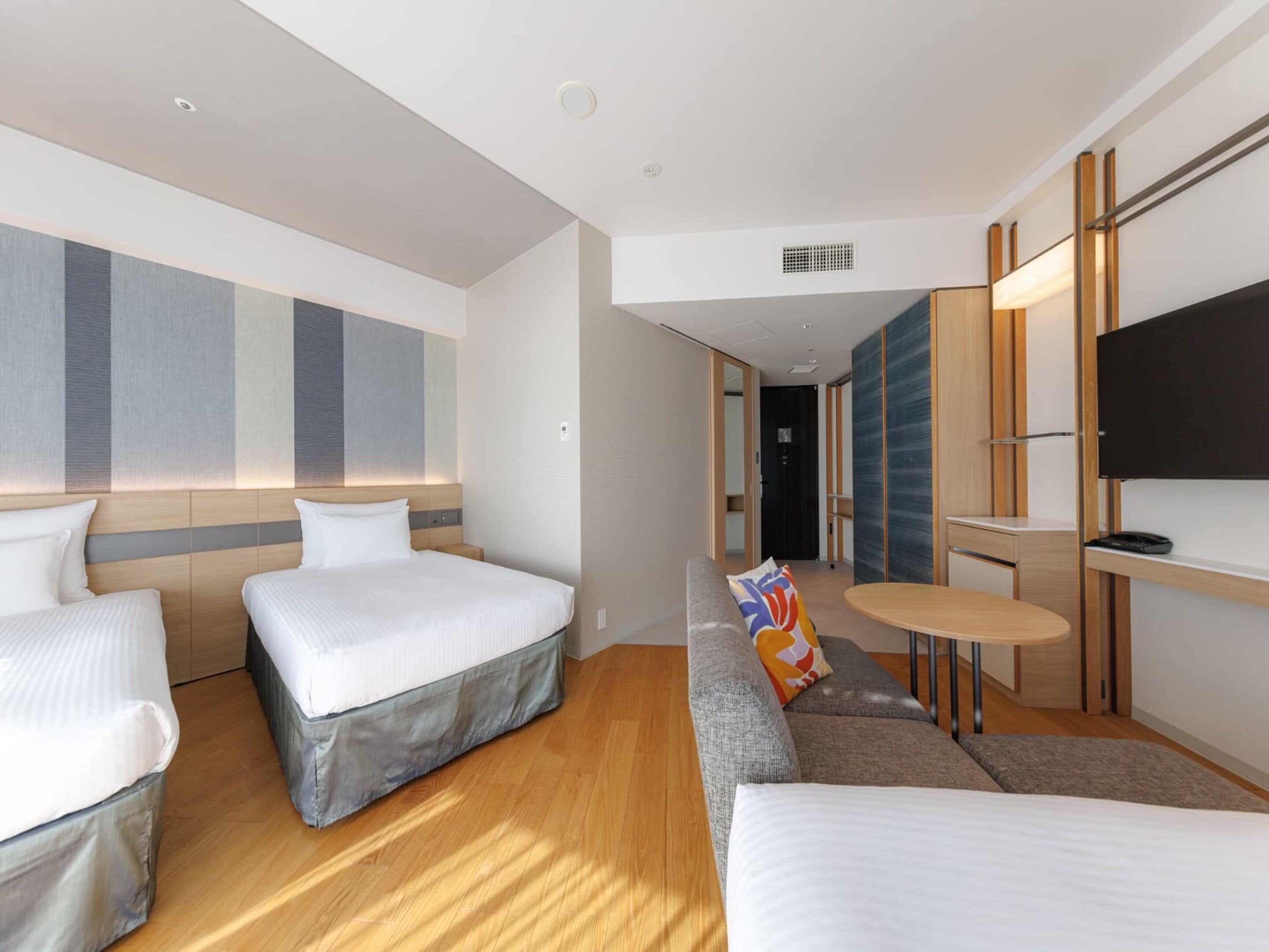 A modern hotel room with two beds, a sofa, a small table, and a TV.