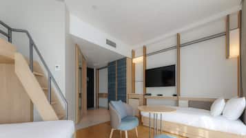 Een moderne hotelkamer met een houten wenteltrap, een bank, een klein rond tafeltje en een aan de muur bevestigde televisie.