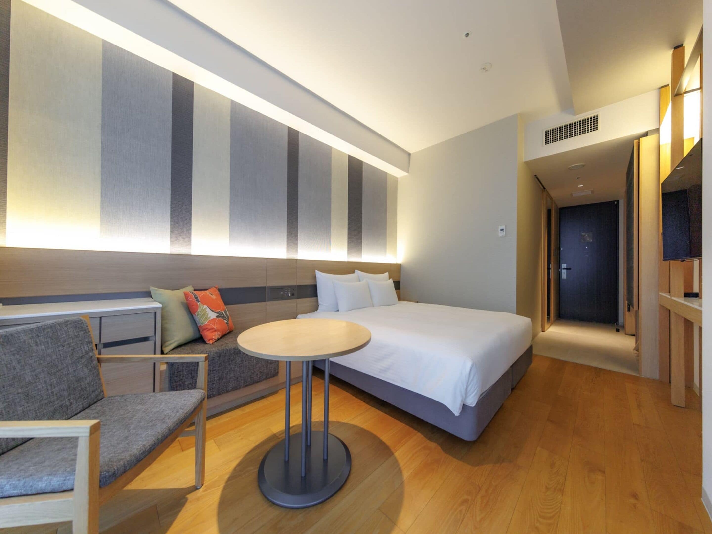 A modern hotel room with a large bed, a seating area with a table, and a large wall with vertical stripes.
