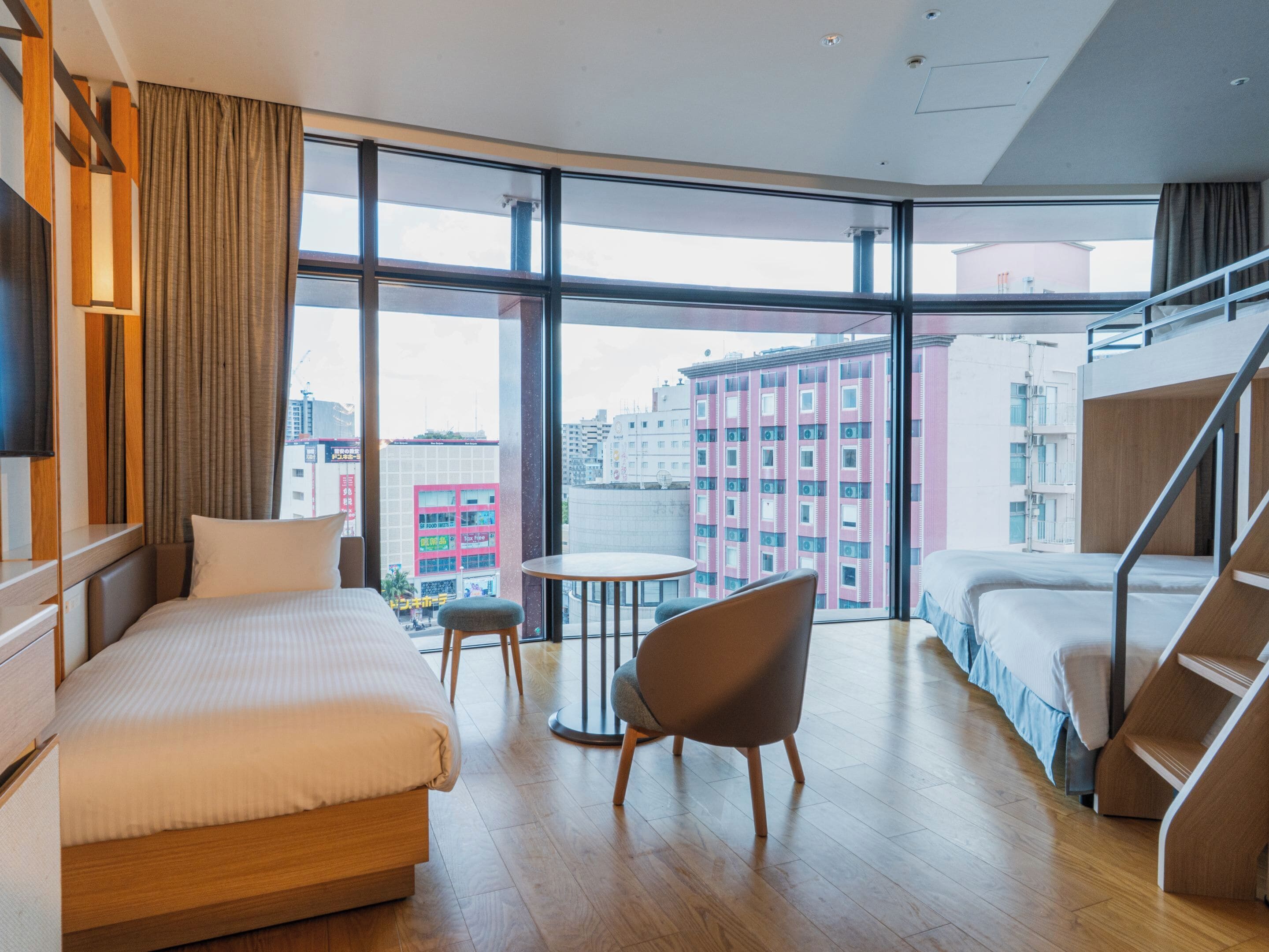 Una habitación de hotel moderna con un ventanal grande, una cama, una silla y una mesita.