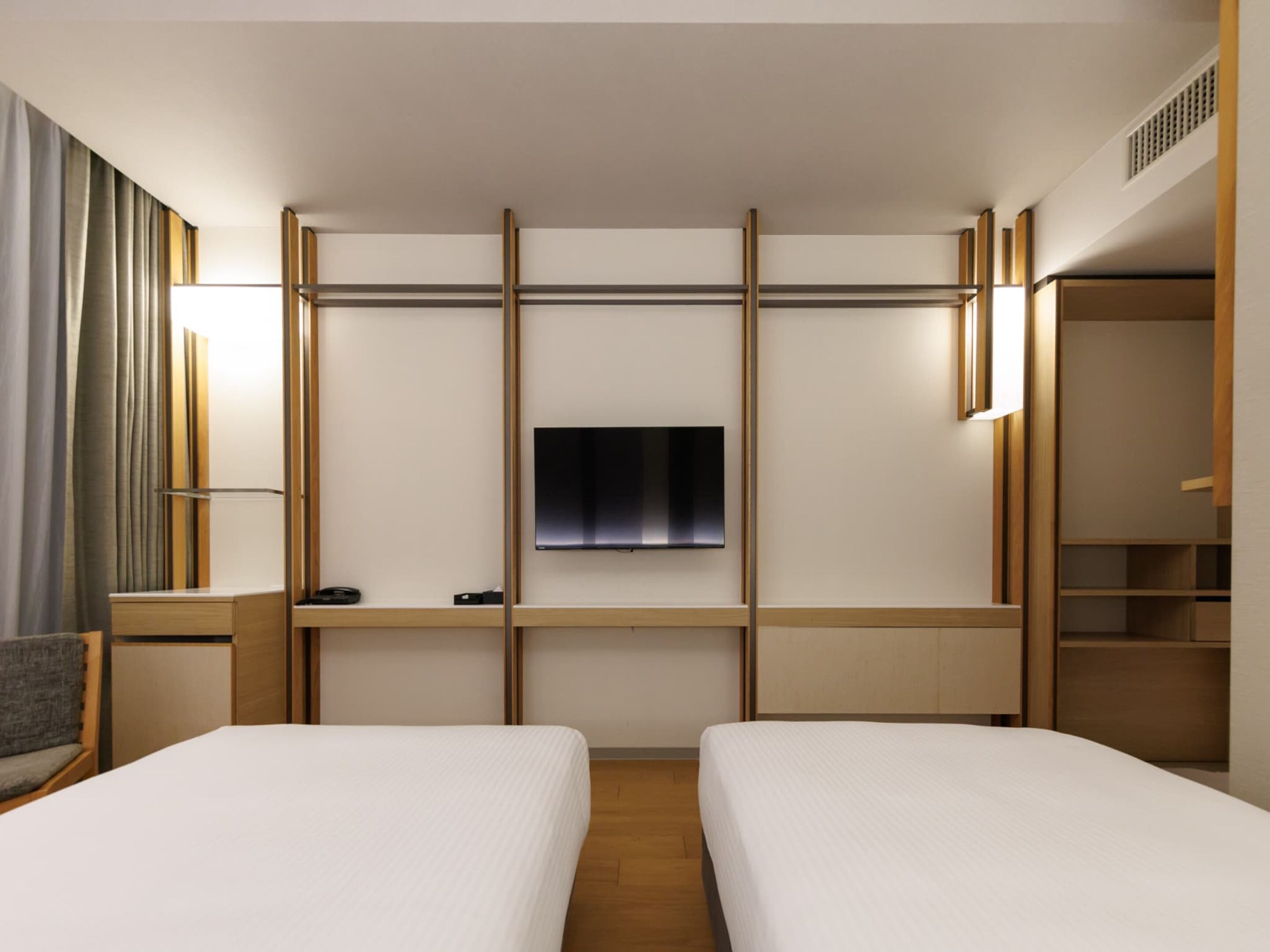 A hotel room with two beds, a TV mounted on the wall, and a wardrobe.