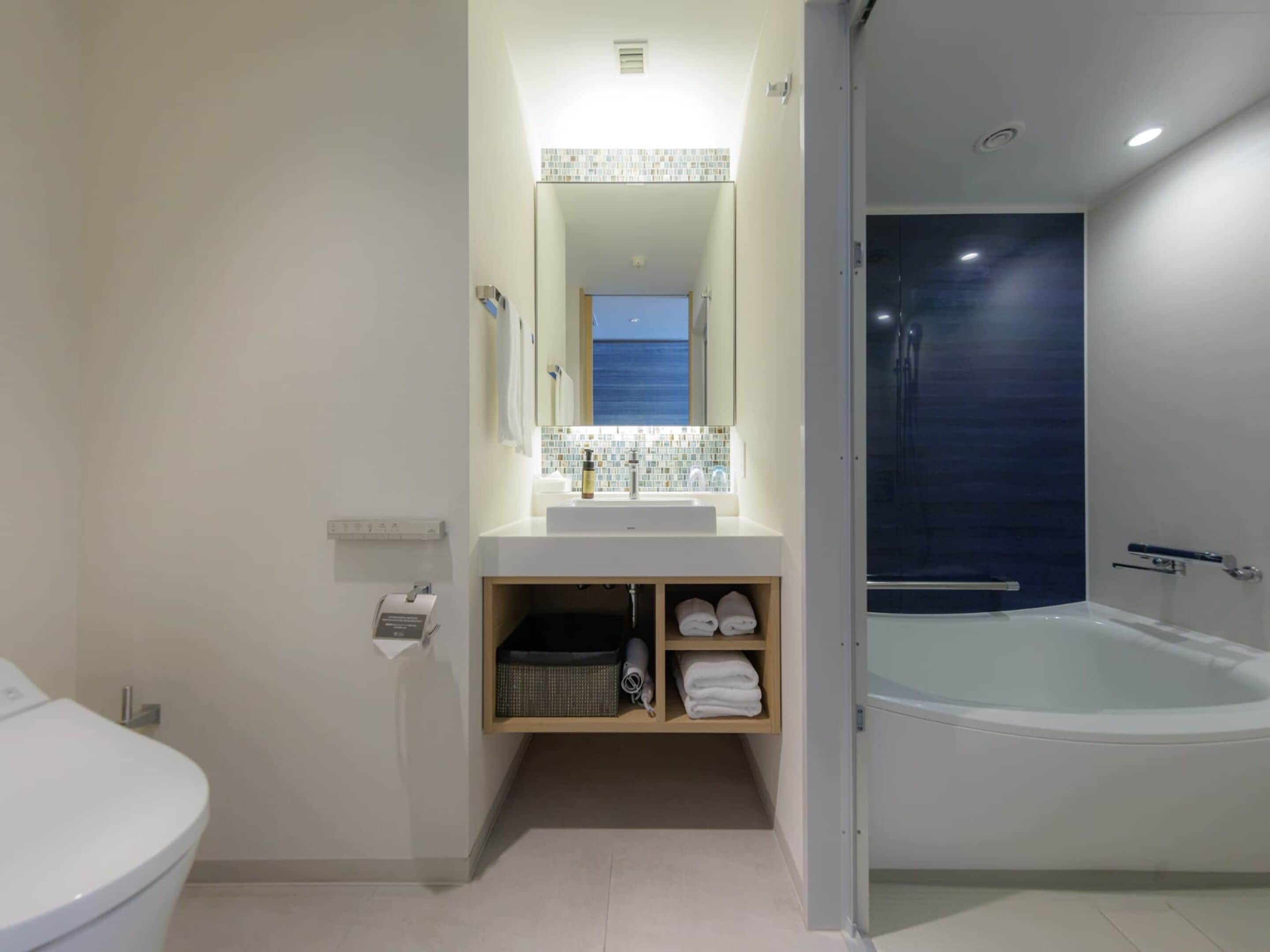 Un baño moderno con lavabo blanco, espejo y una bañera grande.