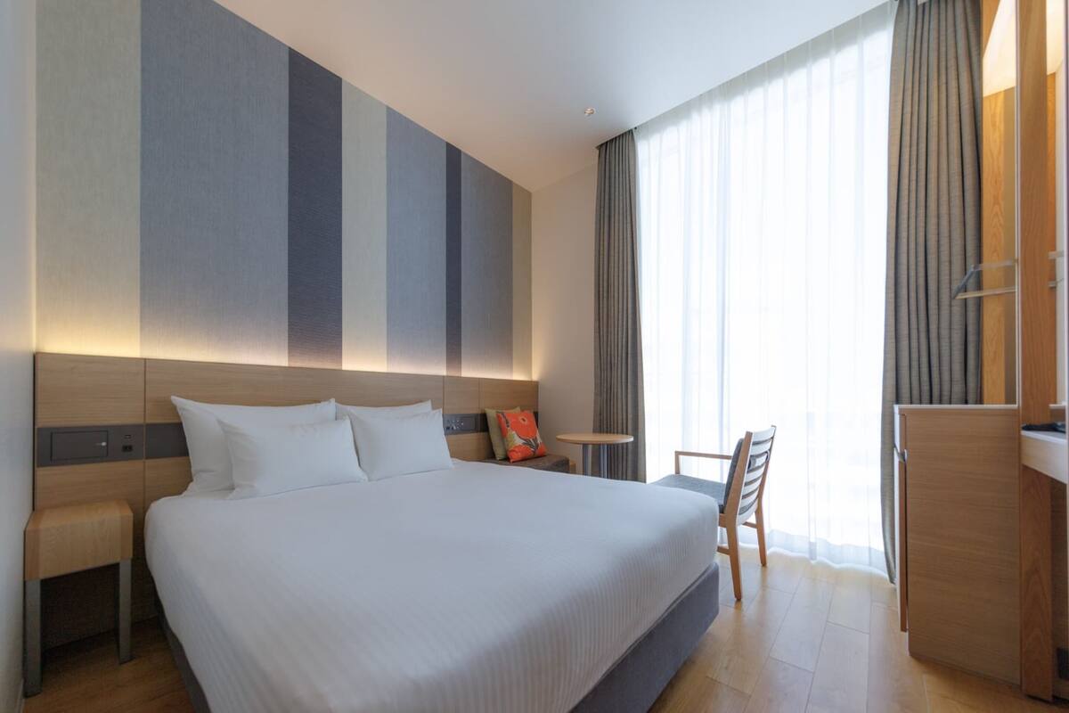 Una habitación de hotel moderna con una cama grande, una mesita de noche, un escritorio y una silla.