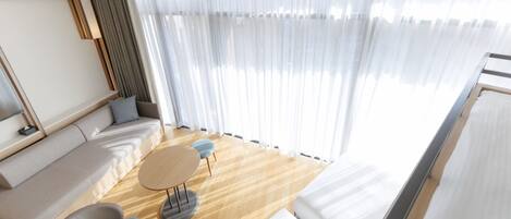 A modern living room with a sofa, chairs, a small round table, and a large window with sheer curtains.