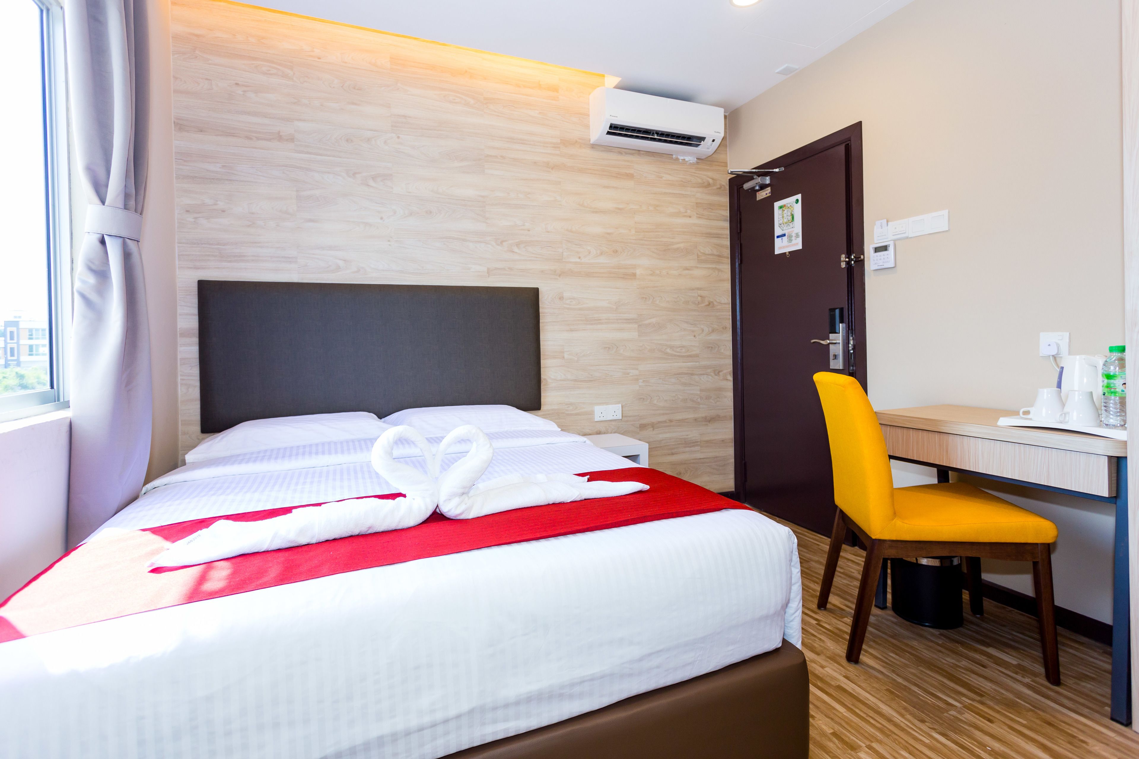 A hotel room with a bed, a desk, a chair, and an air conditioning unit.