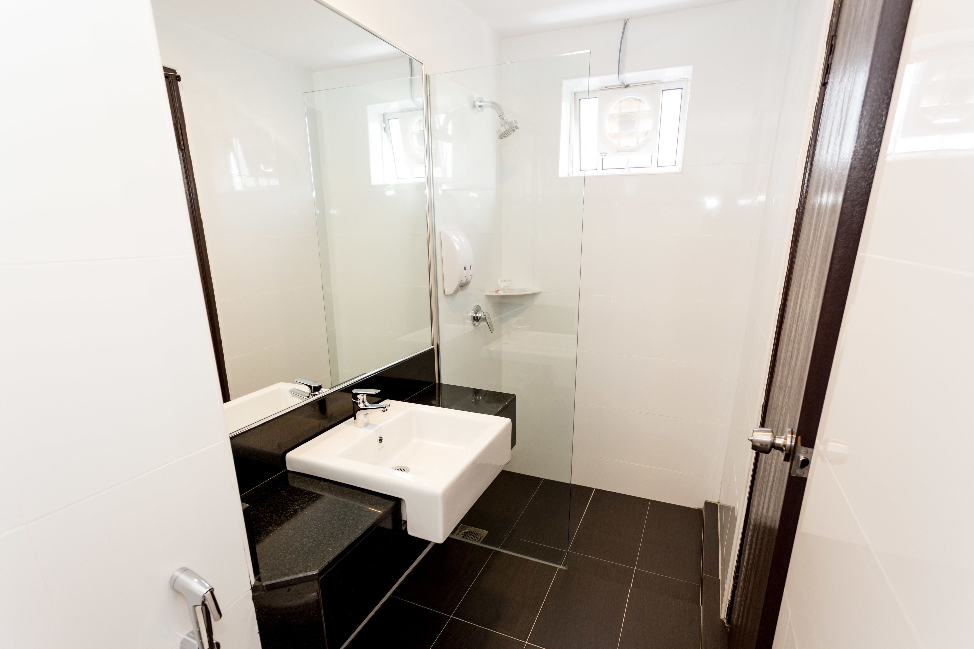 A modern bathroom with a white sink, black countertop, and a glass shower enclosure.