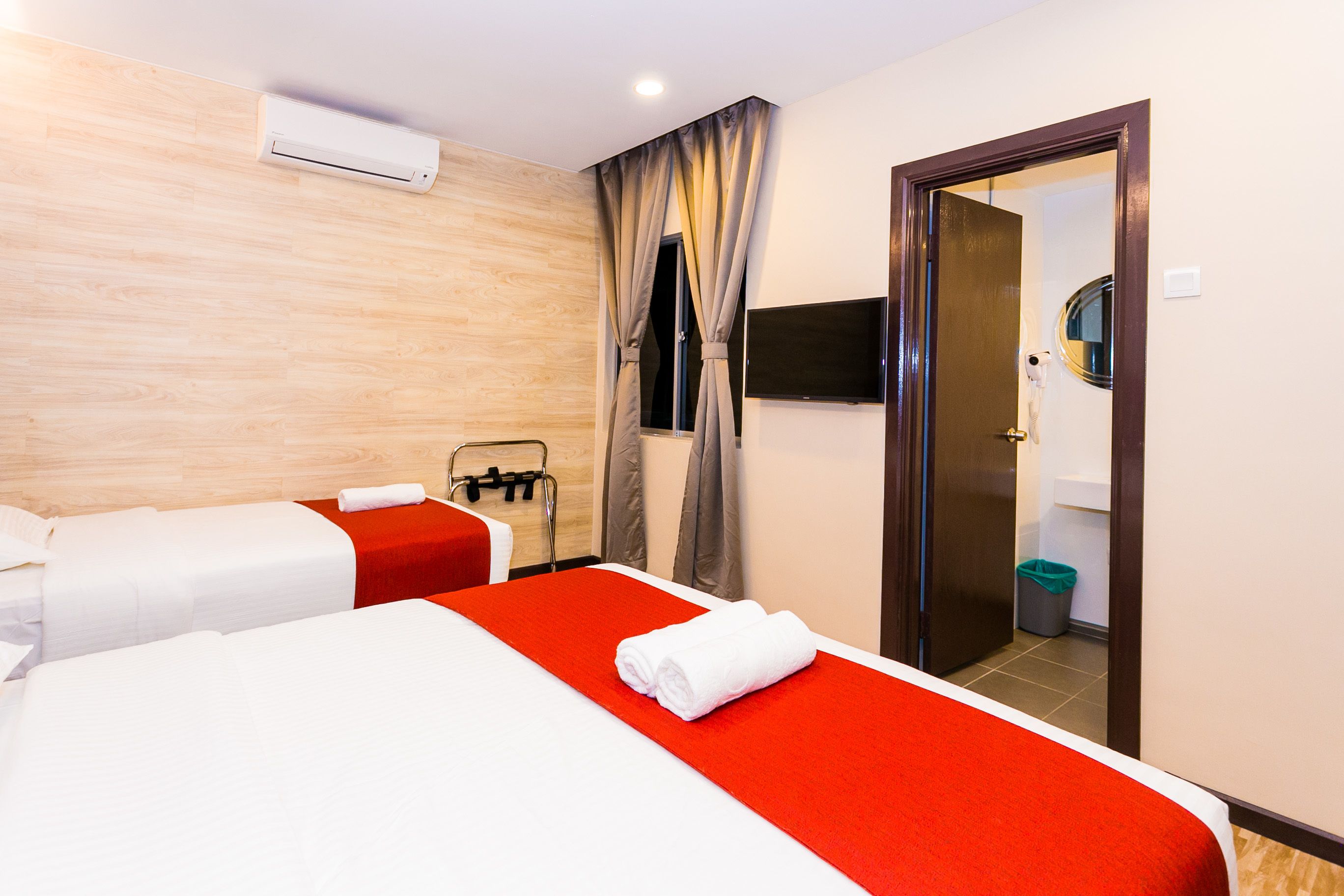 A hotel room with two beds, a TV, a mirror, and a bathroom visible through an open door.