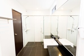 A modern bathroom with a dark tiled floor, a white sink, a large mirror, and a glass-enclosed shower area.