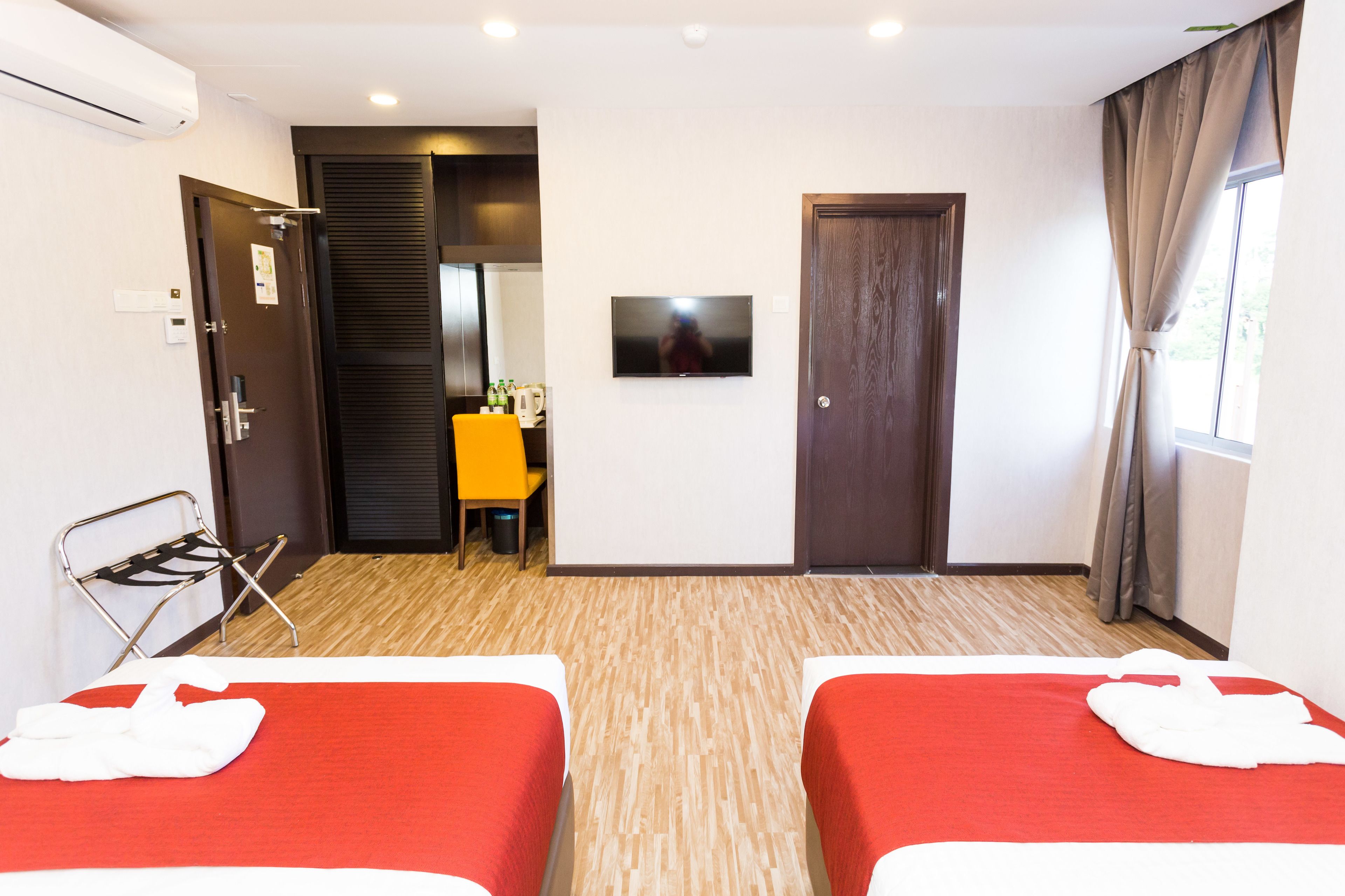 A hotel room with two beds, a TV, a small table with drinks, and a window with curtains.