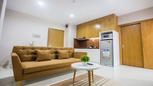 A modern living room with a sofa, a small round table with a plant, a refrigerator, and wooden cabinets. - GK Garden Apartment (Ho Chi Minh City)