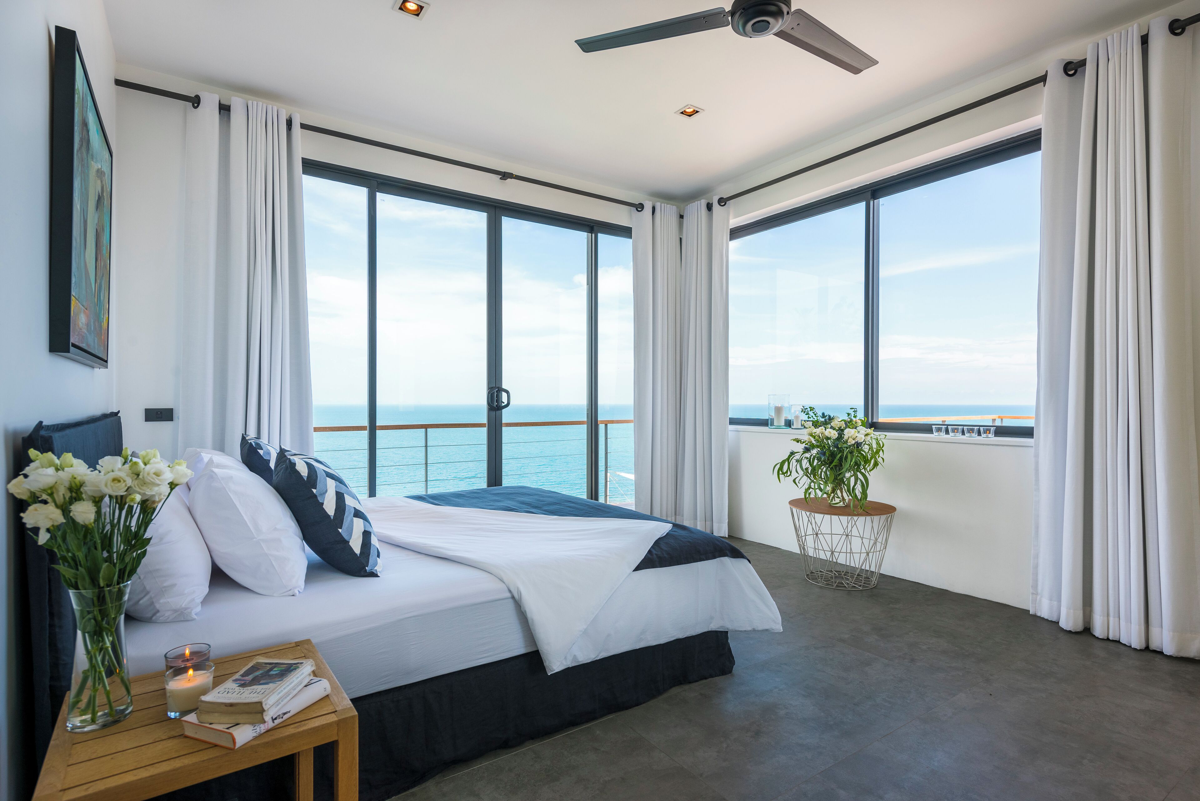 Un dormitorio moderno con una cama grande, un ventilador de techo y vistas al océano.