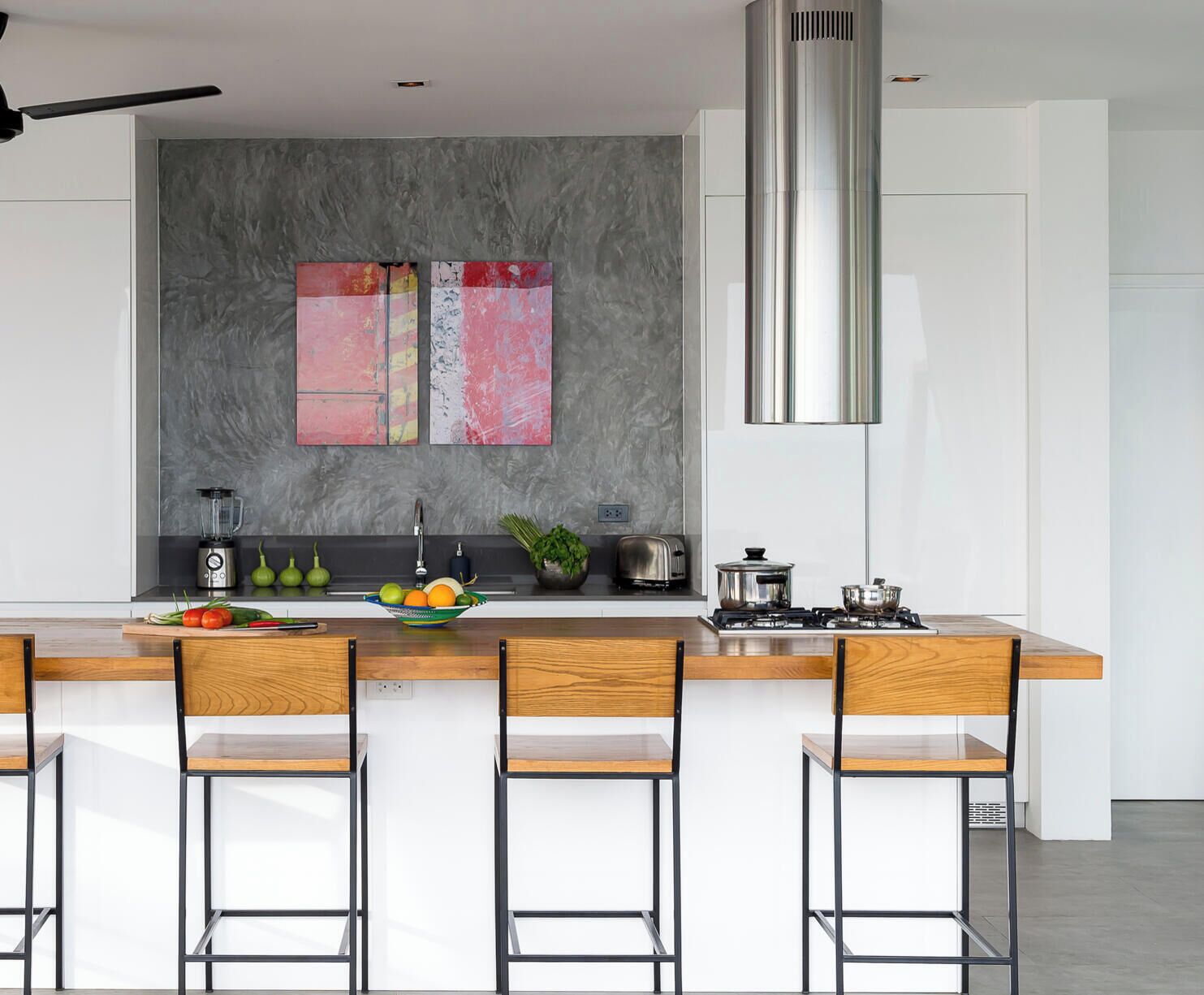 Una cocina moderna con una isla central, taburetes de bar, una campana extractora de acero inoxidable y un salpicadero gris con arte abstracto.