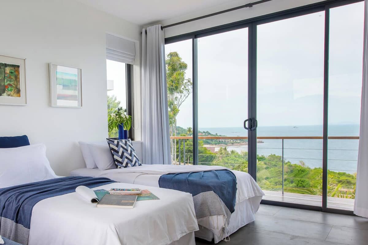 Une chambre avec deux lits, de grandes fenêtres et une vue sur la mer.