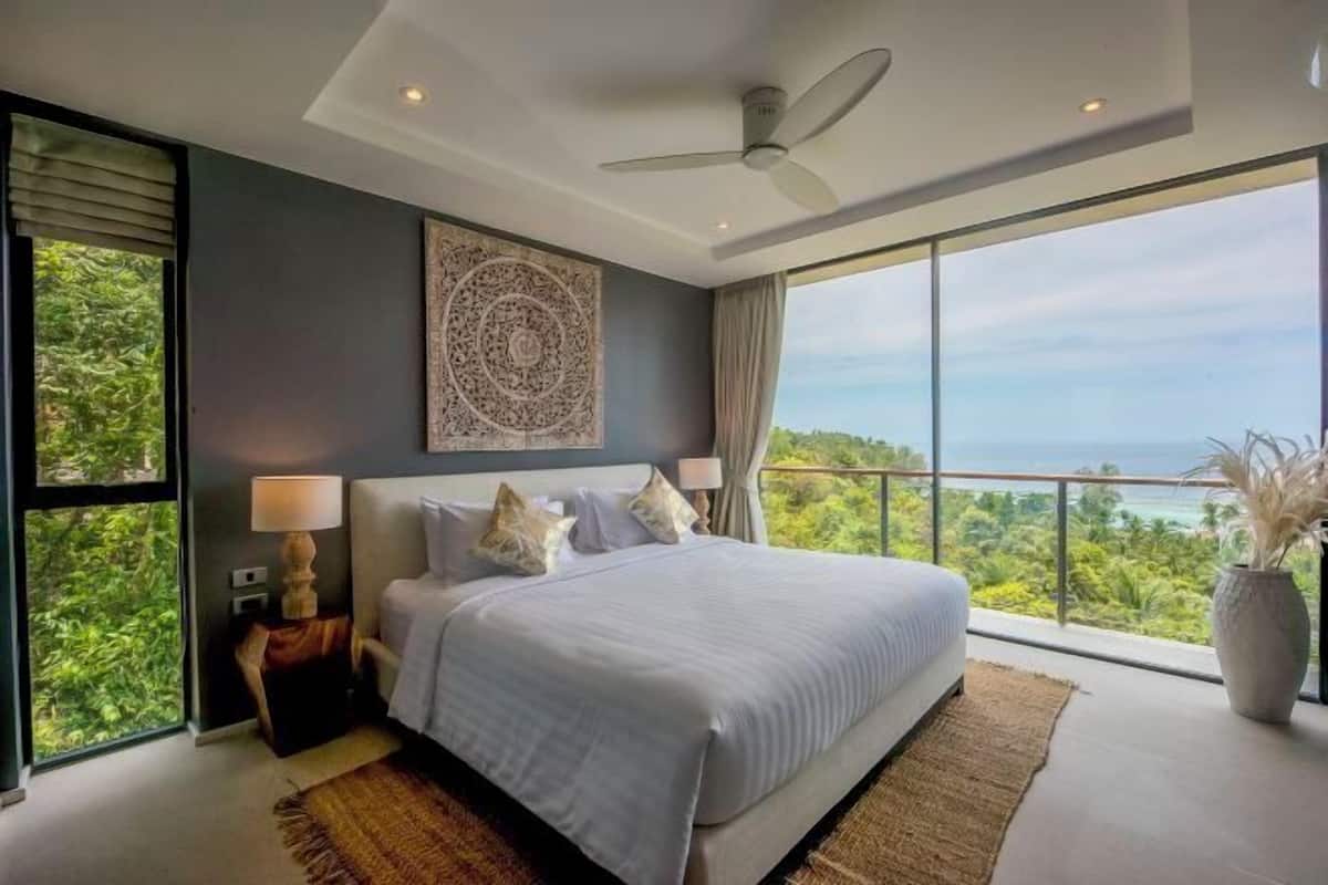 Une chambre dotée d’un grand lit, d’un ventilateur de plafond, d’une vue sur l’océan et d’un élément décoratif mural.