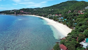 A coastal area with a sandy beach, clear blue water, and lush green hills in the background. - Bay Villas Koh Phangan (Ko Pha-ngan)