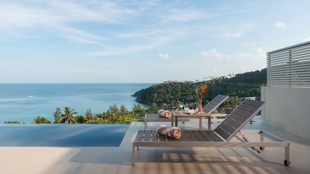 A balcony with two lounge chairs, a table, and a view of the sea and greenery. - Bay Villas Koh Phangan (Ko Pha-ngan)