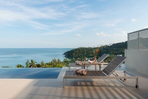 Un balcon avec deux fauteuils, une table et une vue sur la mer et la verdure.