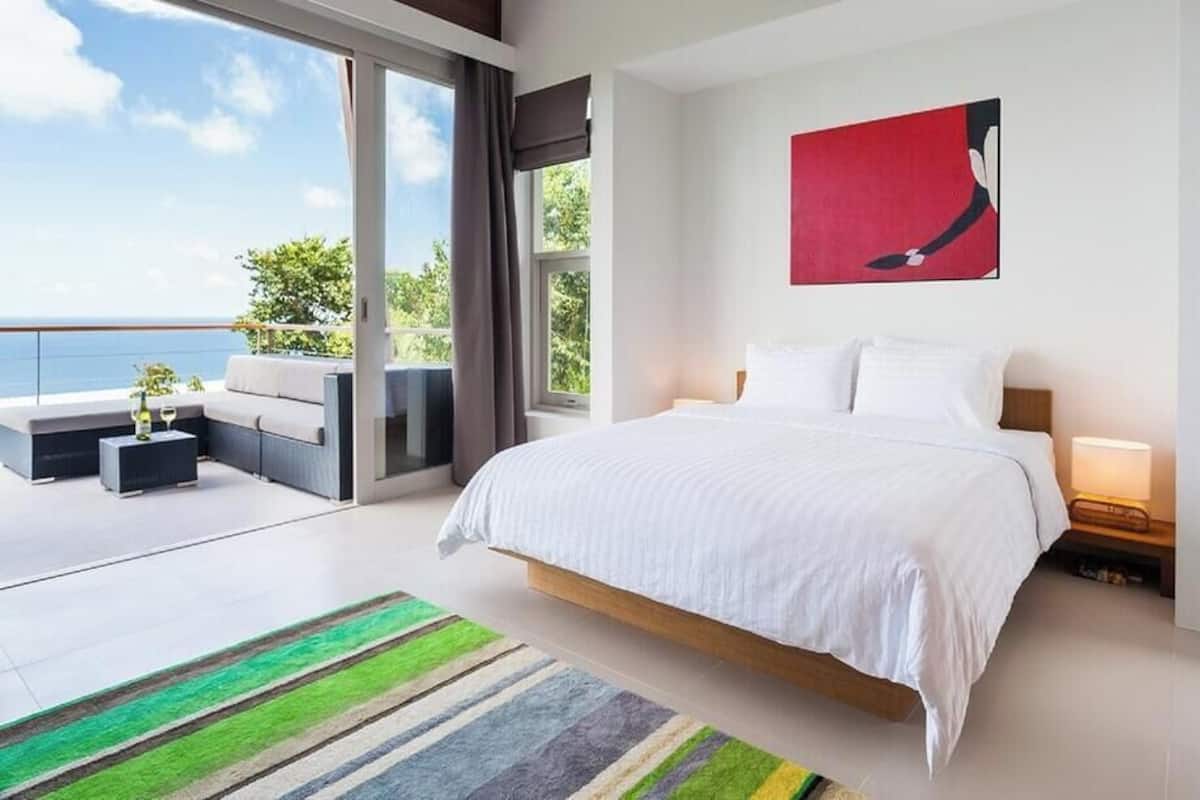 Une chambre moderne avec un grand lit, une vue sur la mer et un balcon avec un espace salon extérieur.