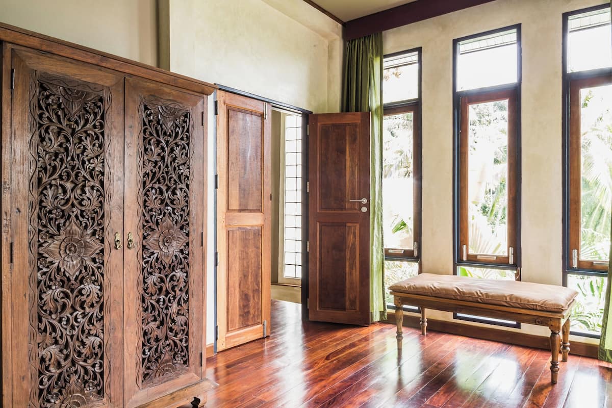 Une pièce comprenant un buffet en bois orné de sculptures complexes, un banc et de grandes fenêtres avec des rideaux.