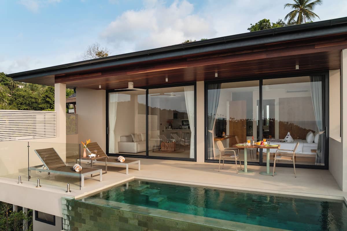 Une maison moderne dotée d’un patio entièrement vitré, d’une piscine et d’un coin repas aménagé avec du mobilier d’extérieur.