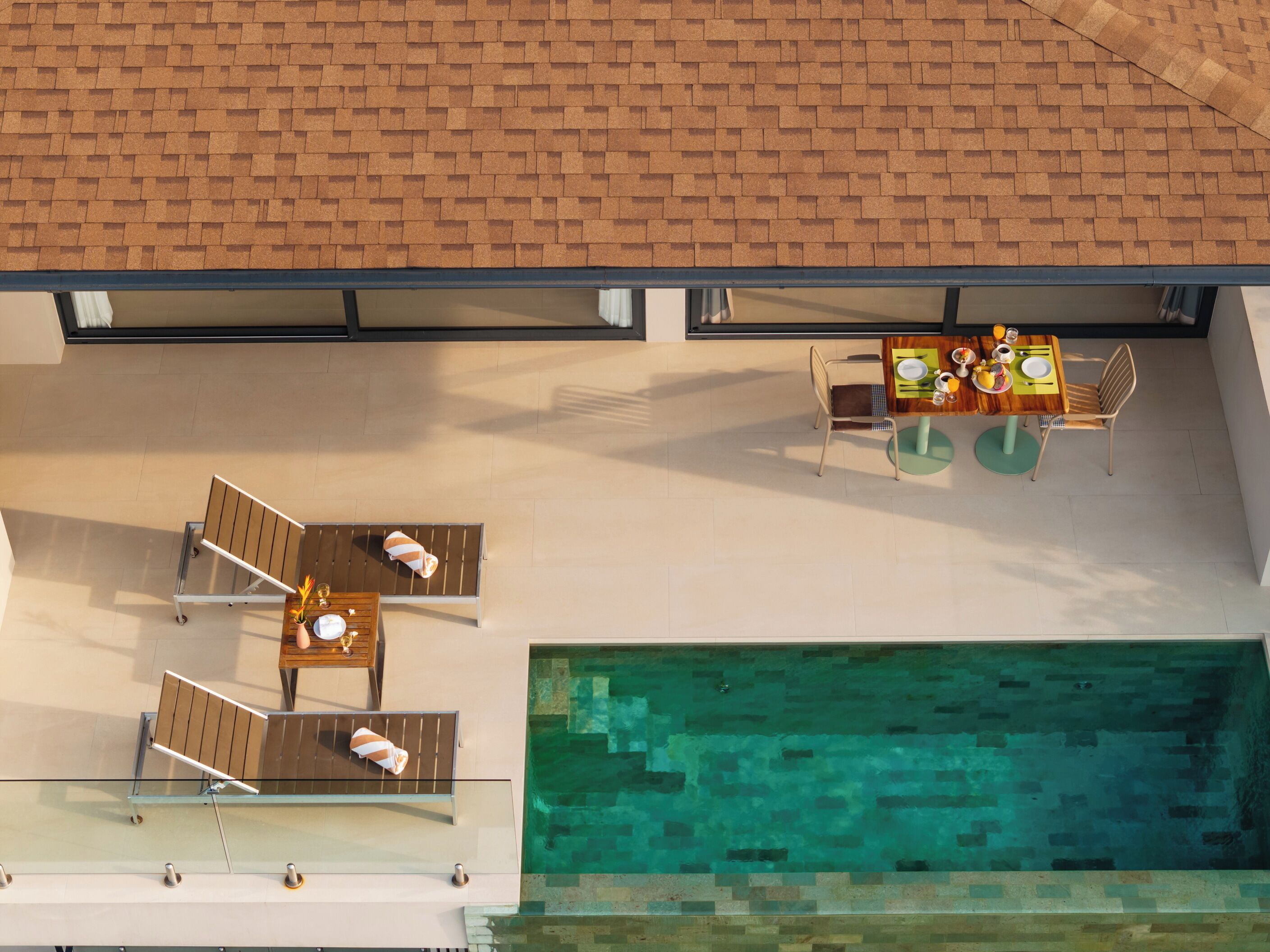 An aerial view of a modern building with a swimming pool, outdoor seating, and a dining area.