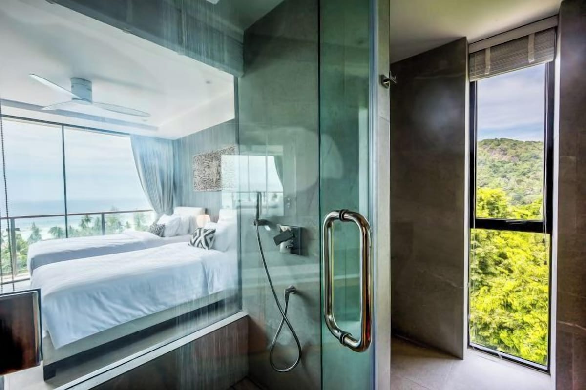 Een moderne hotelkamer met een groot bed, een douchecabine van glas en uitzicht op het omliggende landschap.