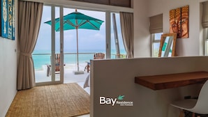 A modern room with a large sliding glass door leading to a balcony with a view of the ocean. There is a wooden desk and a chair, a ceiling fan, and artwork on the walls. - Bay Villas Koh Phangan (Ko Pha-ngan)