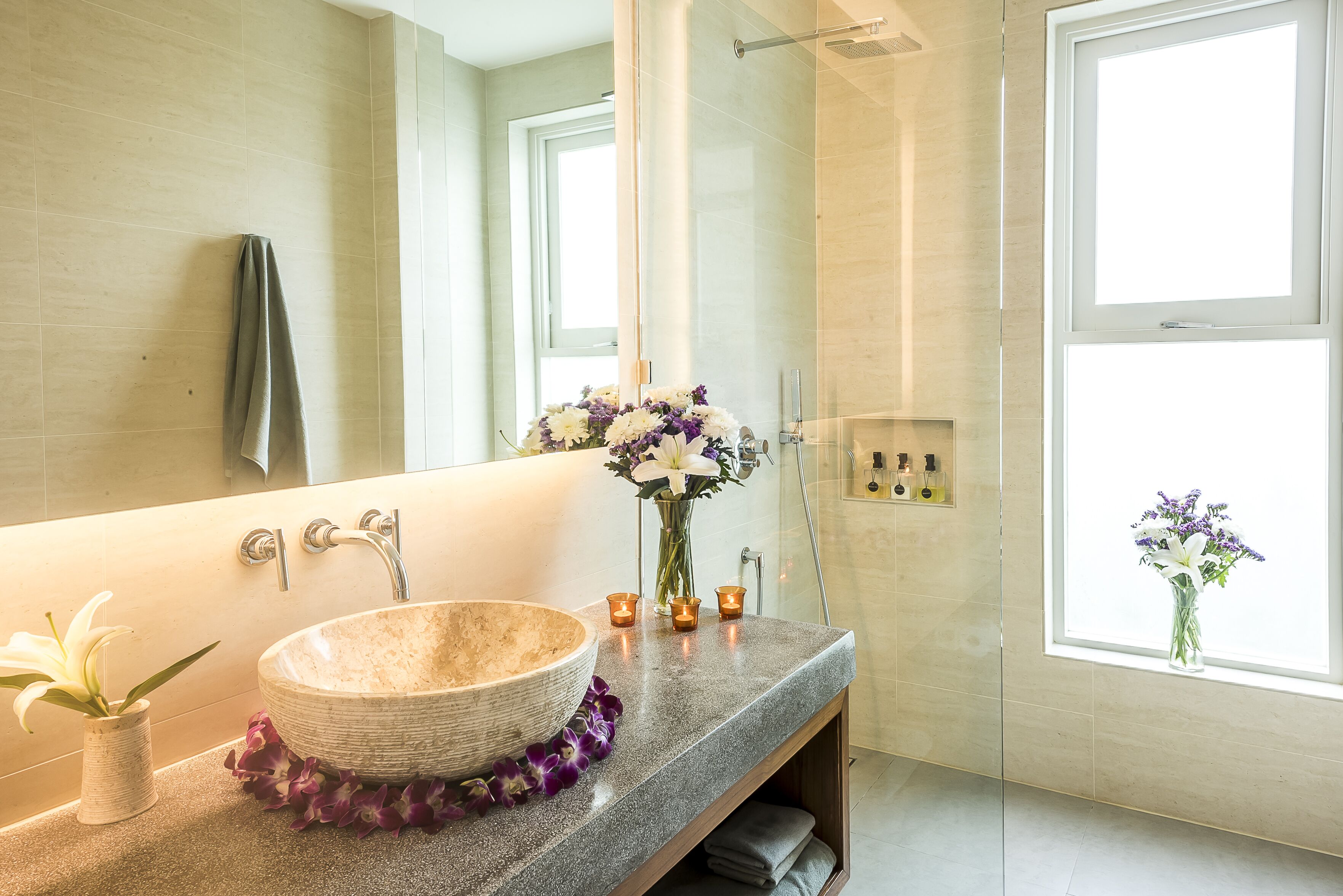 A bathroom with a large mirror, a beige sink, and a window with a view.