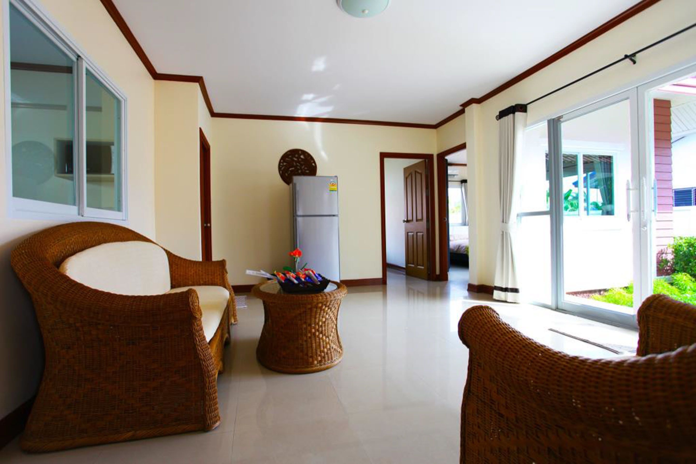 A spacious living area with wicker furniture, a refrigerator, and a sliding glass door leading to an outdoor area.