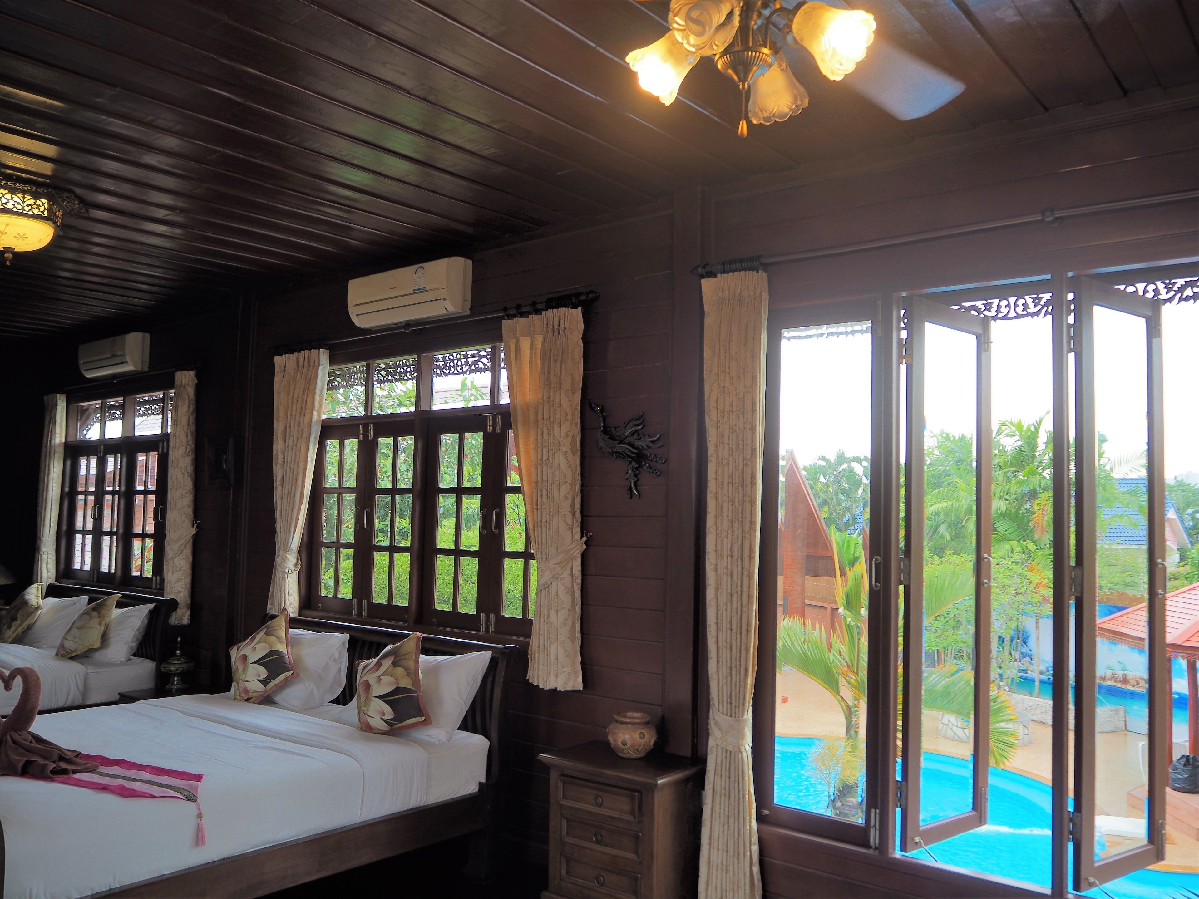 A room with a bed, a nightstand, and a window with a view of a pool and greenery.