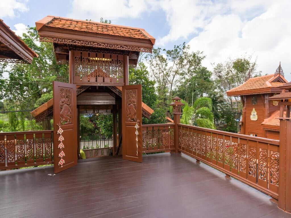 A wooden bridge with intricate railings and a traditional roof design, leading to a building with a tiled roof.