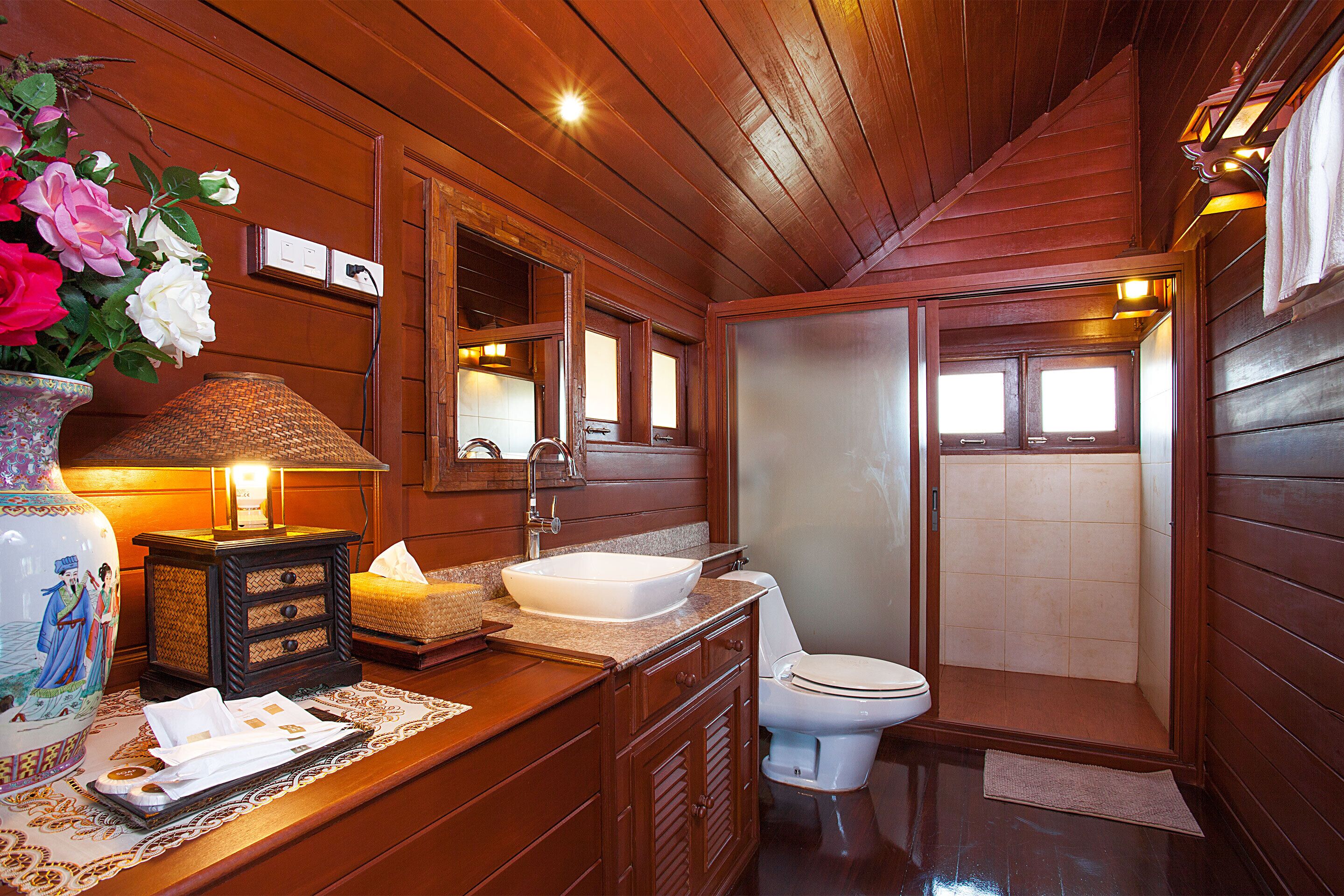 A wooden bathroom with a sink, toilet, and shower.