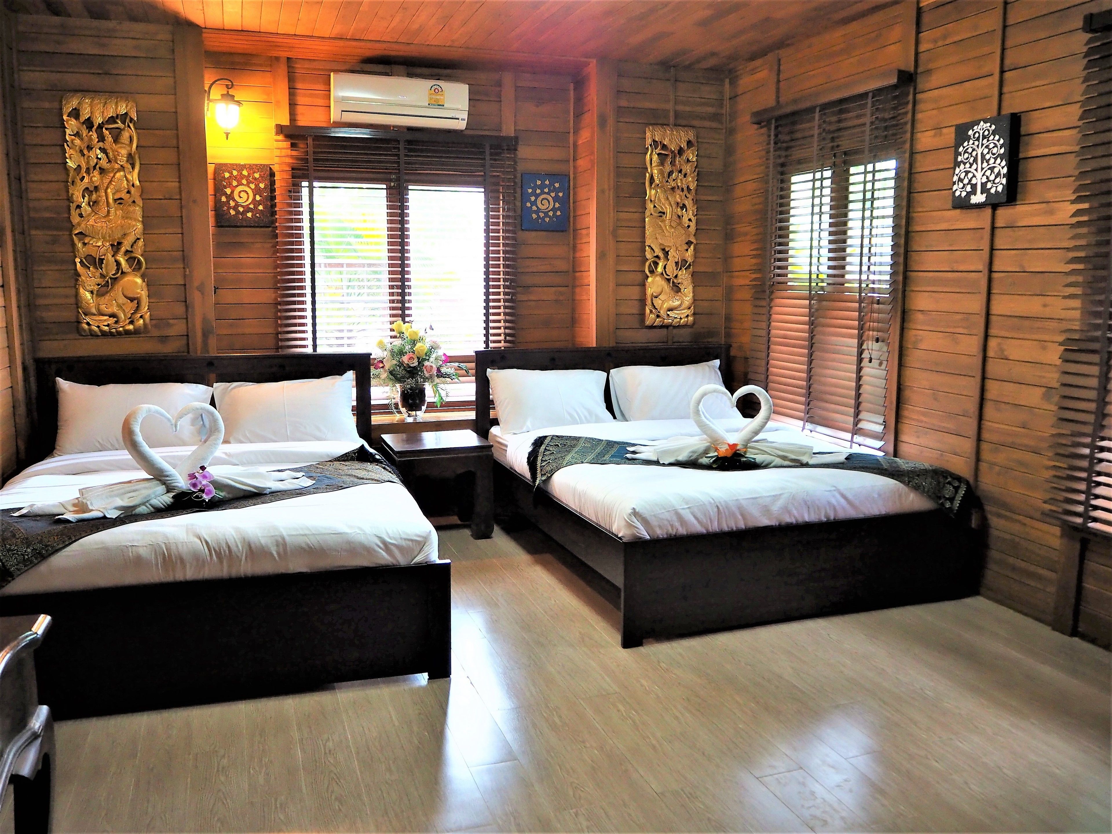 A wooden room with two beds, each with heart-shaped towels and a vase of flowers.